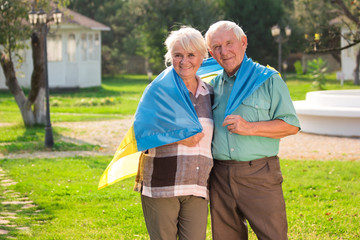 Elderly couple with Ukrainian flag. Smiling people on park background. The happy Ukrainians.