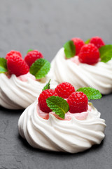Mini  Pavlova meringue nests with raspberries and mint on black stone background