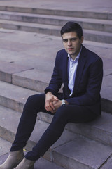 Handsome young man with styled hair. The man is sitting on the steps. 