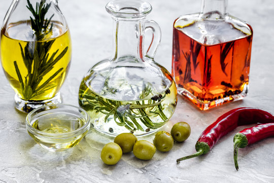 Bottles with pumpkin, chili and olive oils and herbs on stone background