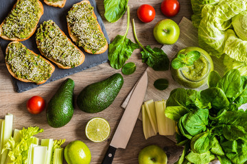 Detox diet. Green smoothie and sanwiches with avocado. Different vegetables on wooden background