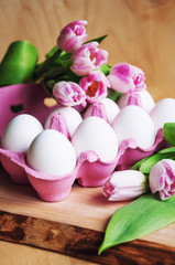 Easter greeting card with eggs in a carton and pink tulips on wooden background, closeup, selective focus