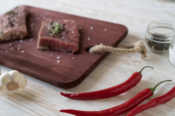 Fresh raw steaks with rosemary, pepper and garlic on wooden desk