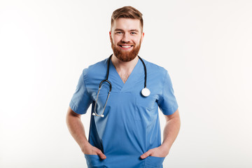 Smiling male doctor standing with stethoscope and holding hands in pockets