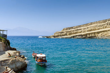 Obraz premium Blue lagoon with fishing boat and rock with caves on a background near Matala town on Crete island, Greece