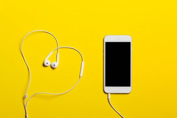 Close-up of smart phone with headphones on a yellow background. (Top view). Listen to music.