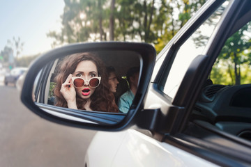 Reflection of a cheerful beautiful girl in a side mirror of a car