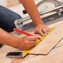 Fototapeta na wymiar Laying ceramic floor tiles - man hands marking tile to be cut, closeup