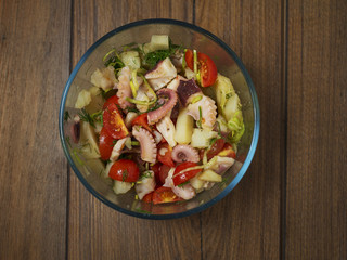 Top view of a fresh octopus salad in a glass bowl on a wooden surface.