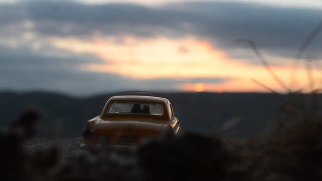 silhouettes of Happy Couple sitting in old vintage car at sunset time. Toy installation effect like reality. Selective focus. Love theme