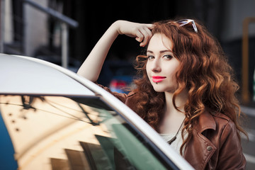Obraz na płótnie Canvas Beautiful young girl with wavy hair leans on the car