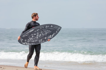 Junger Mann am Strand mit Skimboard, Swakopmund, Südatlantik