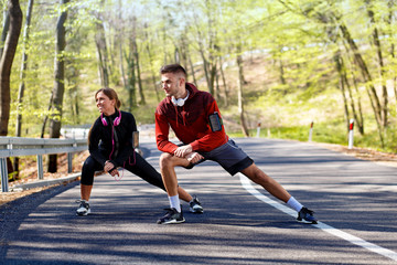 Obraz premium Young man and woman stretching muscles on the road before running. Young couple warming up.