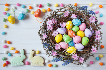 Fototapeta na wymiar Easter nest with eggs and flowers on a light wooden background, candy, cakes