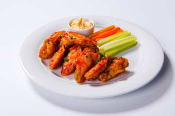 Spicy BBQ buffalo chicken wings sitting on plate garnished with carrot and celery sticks with blue cheese dipping sauce