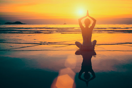 Yoga woman meditation on sunset sea coast with reflection in water.