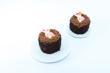 Obraz na płótnie Canvas Two small chocolate cakes with Easter bunny detail on white dishes isolated in white background