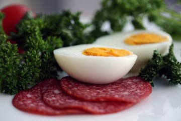 Halves of a boiling egg decorated with salami and parsley; close up, selective focus.