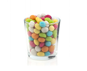A lot of colorful candies in a transparent glass on a white background