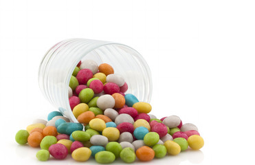A lot of colorful candies in a transparent glass on a white back