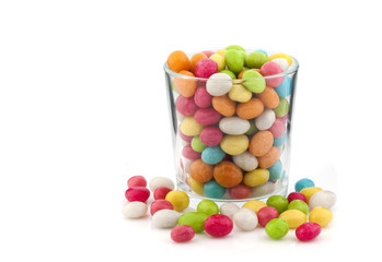 A lot of colorful candies in a transparent glass on a white back