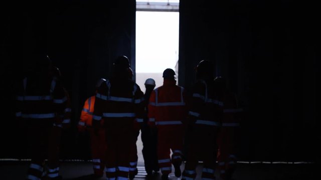  Workers at a fuel plant walking into darkness & preparing to go underground