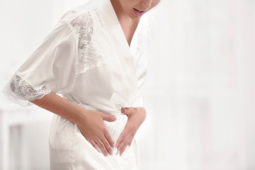 Young woman suffering from abdominal pain at home, closeup. Gynecology concept