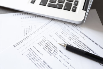 Script code on paper, pen and laptop at workplace of programmer