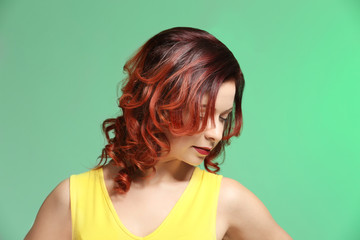 Beautiful young woman with dyed curly hair on color background