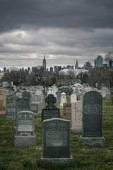 Calvary cemetery gravestones on a dark cloudy day with Manhattan skyscrapers in the background - 143229725