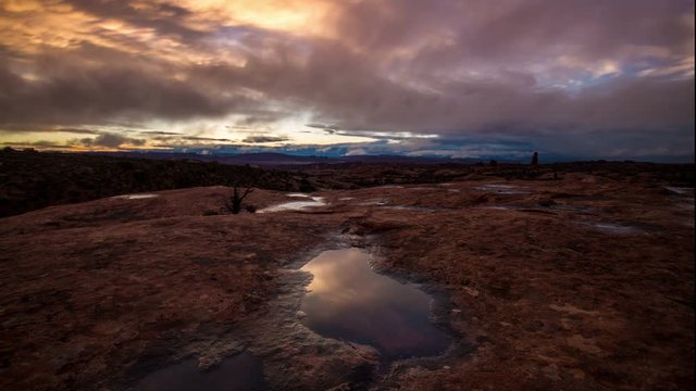 Time-lapse at sunset in Arches National Park reflecting out of a pool of water.