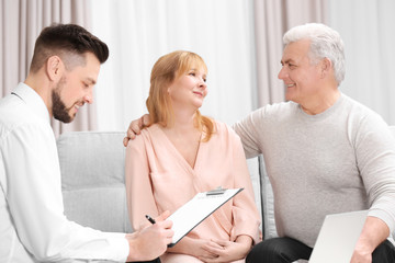 Middle aged couple signing contract sitting on couch at home