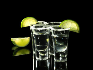 Tequila shots with juicy lime slices and salt on black background