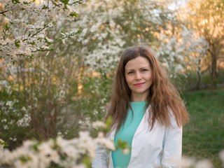 outdoor portrait of a beautiful woman in white jacket among white blossom tree