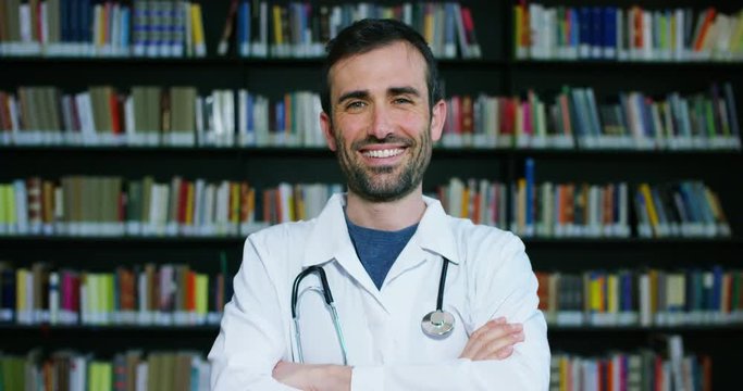 A young and beautiful female doctor in a library smiling happy and holding books after doing a search and after studying. Concept: educational, portrait, library, and medical care and welfare