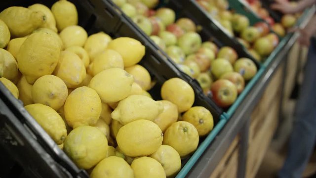Fresh fruit on display in grocery store, hand reaches out to pick up a lemon