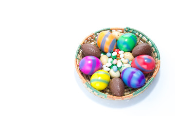 A straw basket with six hand colored and chocolate easter eggs - yellow, blue, green, red, pink, orange with stripes isolated in white background