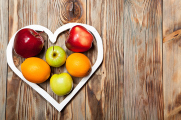 White heart, apples and oranges on the wooden background