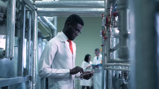 The African scientist standing on a factory and using the tablet. Horizontal indoors shot.