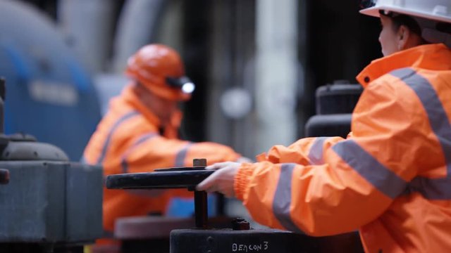  Male & female engineers in power plant turning a valve on pipeline