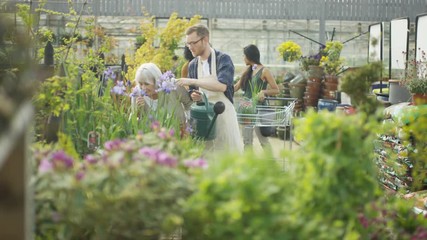  Friendly worker in garden center, watering the plants & talking to customer