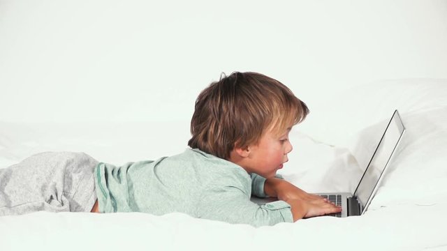 4 j&auml;hriger bub liegt im bett und spielt mit notebook