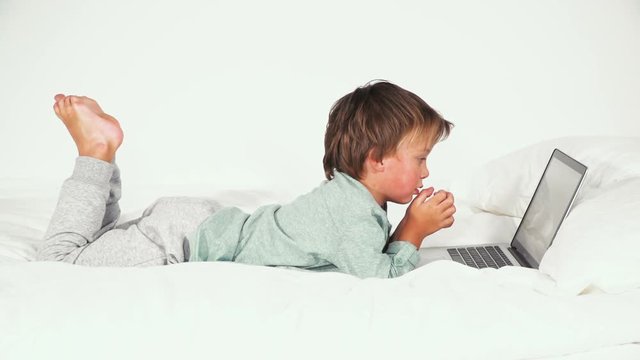 4 j&auml;hriger bub liegt im bett und spielt mit notebook