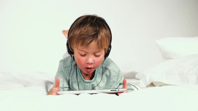 4 j&auml;hriger bub im bett mit kopfh&ouml;rern spielt mit dem tablet