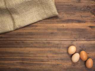 Brown chicken eggs lay on a piece of burlap on a wooden table from the old boards. Top view. Three fresh chicken eggs close-up, background for advertising or Easter greetings, rustic style