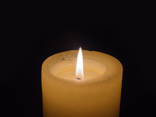 Large, burning, wax candle on a dark background with flaming, burning fuse, close-up photo with soft, blurred focus.