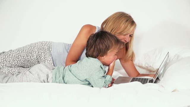 4 j&auml;hriger bub liegt mit seiner mutter im bett und spielt mit notebook