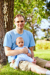Naklejka na ściany i meble Happy father sitting with newborn son on grass