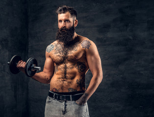 Obraz na płótnie Canvas Shirtless bearded male with tattooed torso doing workout with dumbbell.