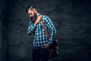 Bearded male with tattoo on arm, dressed in a blue fleece shirt holds backpack.